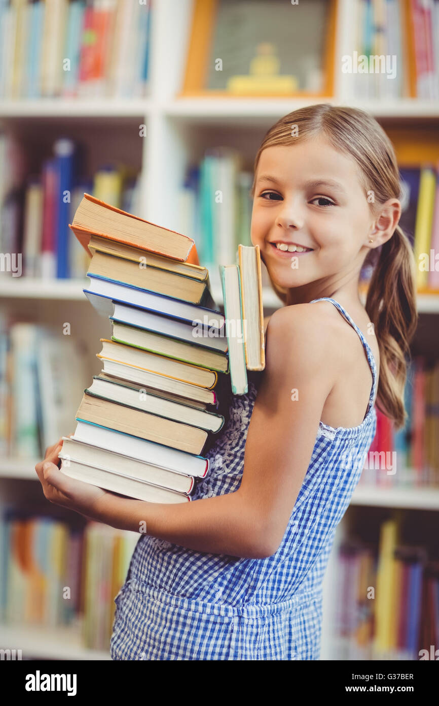 Schulmädchen mit Stapel Bücher in der Bibliothek Stockfoto