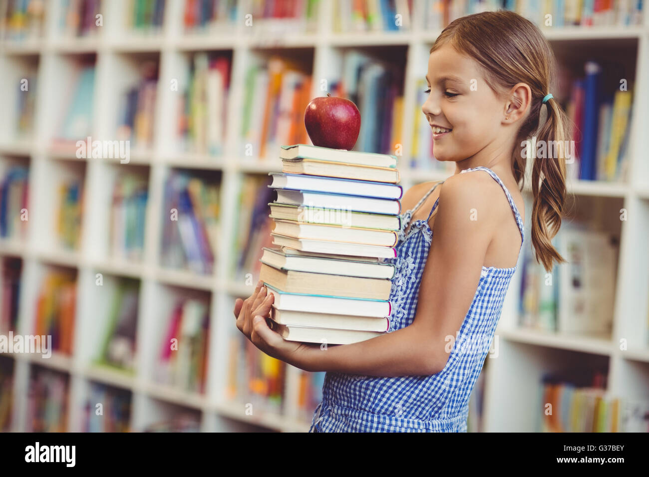 Schulmädchen mit Stapel Bücher in der Bibliothek Stockfoto
