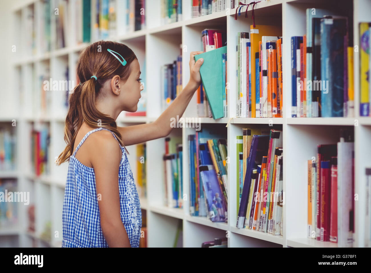 Schulmädchen, das ein Buch aus Regal in Bibliothek Stockfoto