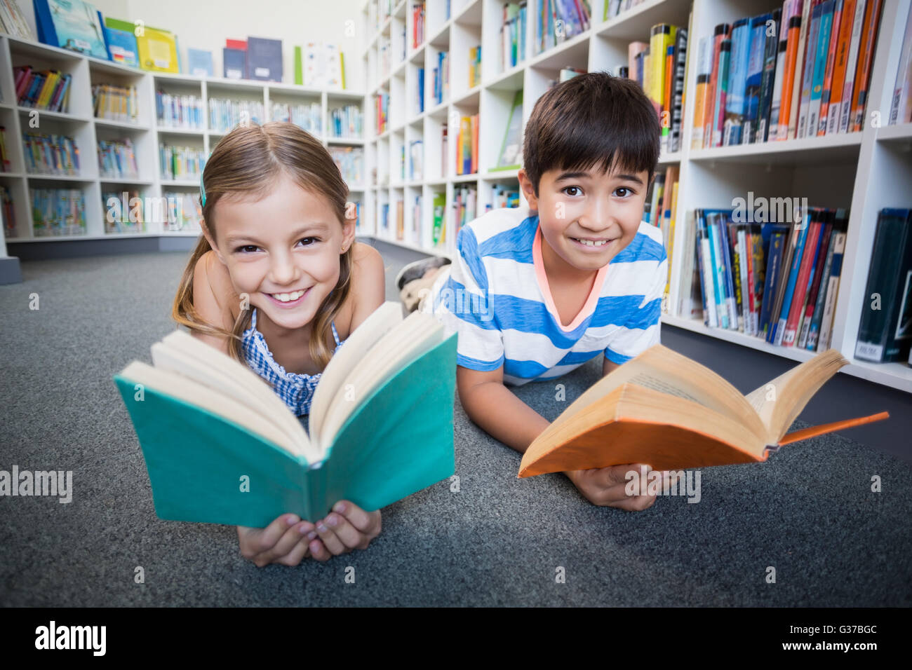 Glückliche Schulkinder am Boden liegen und ein Buch in der Bibliothek Stockfoto