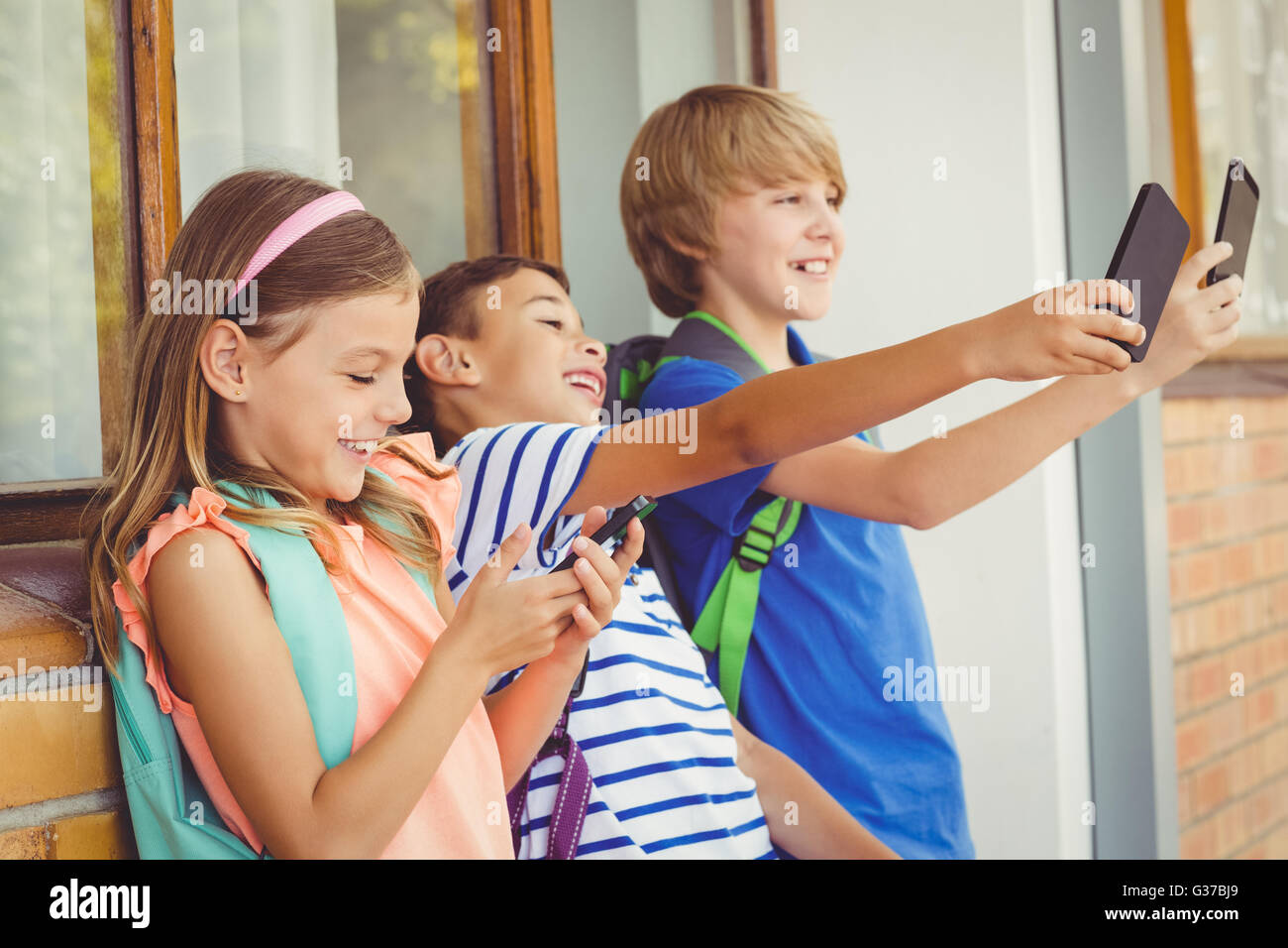 Schulkinder unter Selfie und mit Handy im Korridor Stockfoto