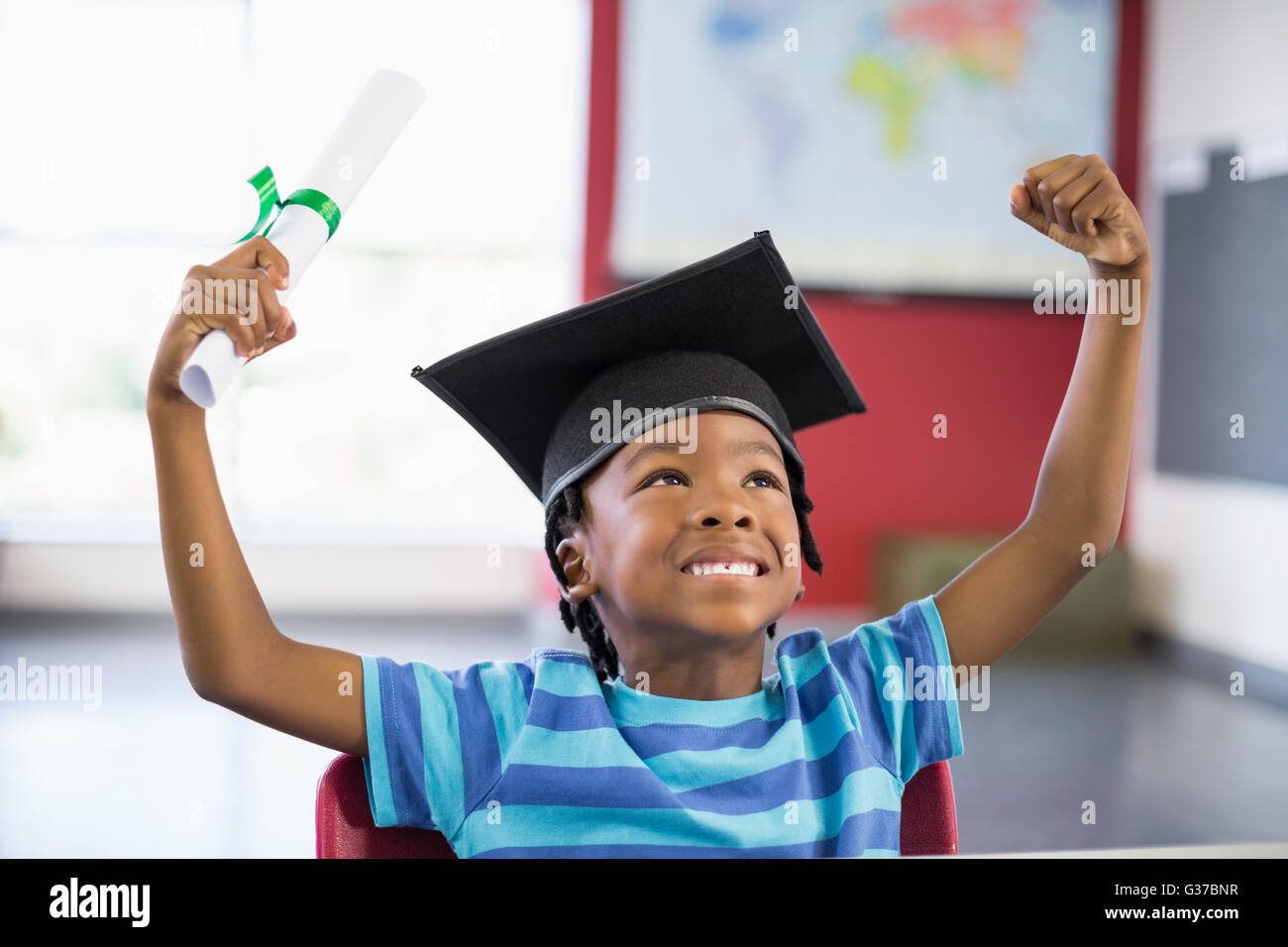 Aufgeregt Schuljunge in Doktorhut mit Zertifikat im Klassenzimmer Stockfoto
