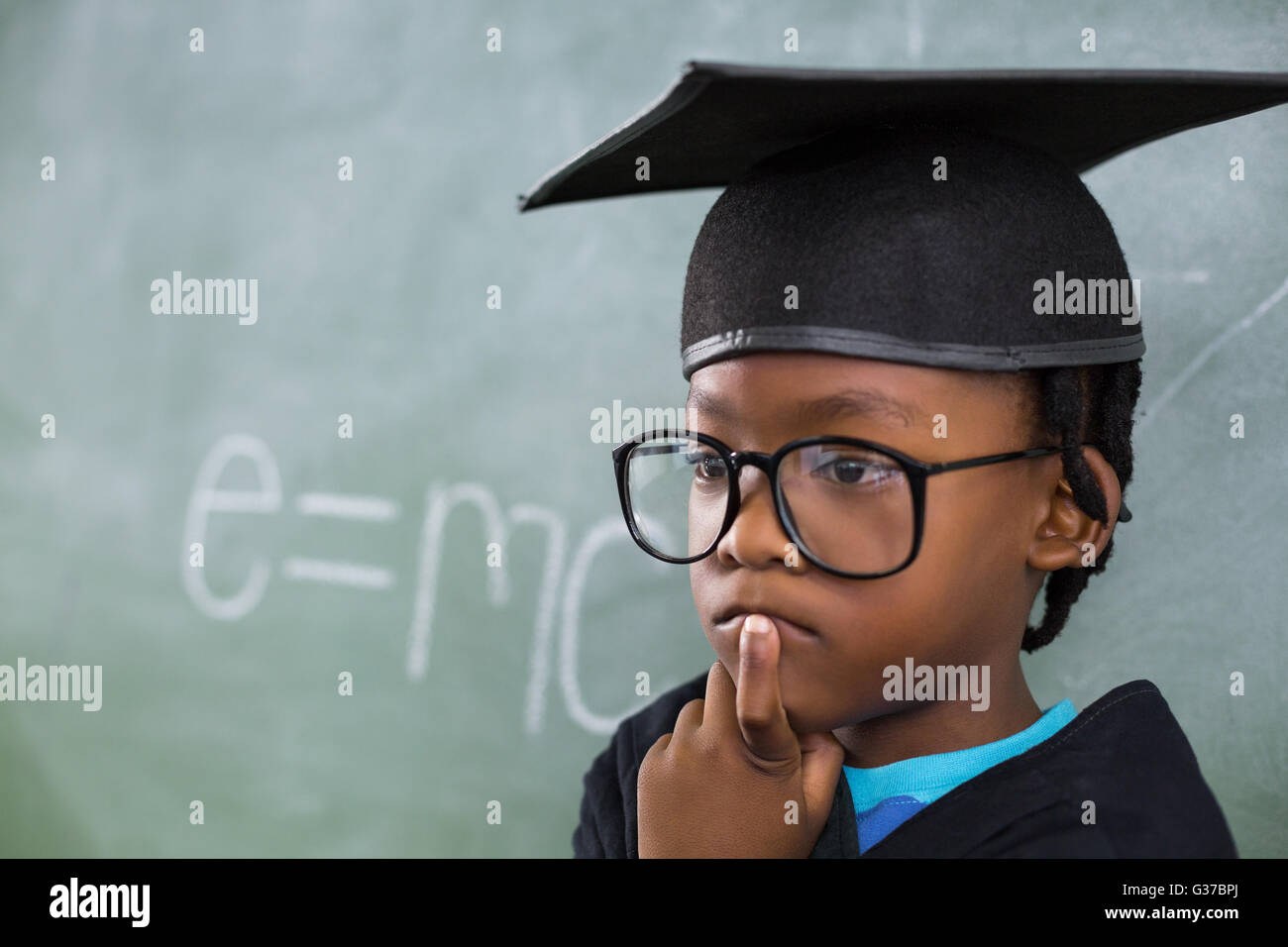 Nachdenkliche Schüler tragen Doktorhut im Klassenzimmer Stockfoto
