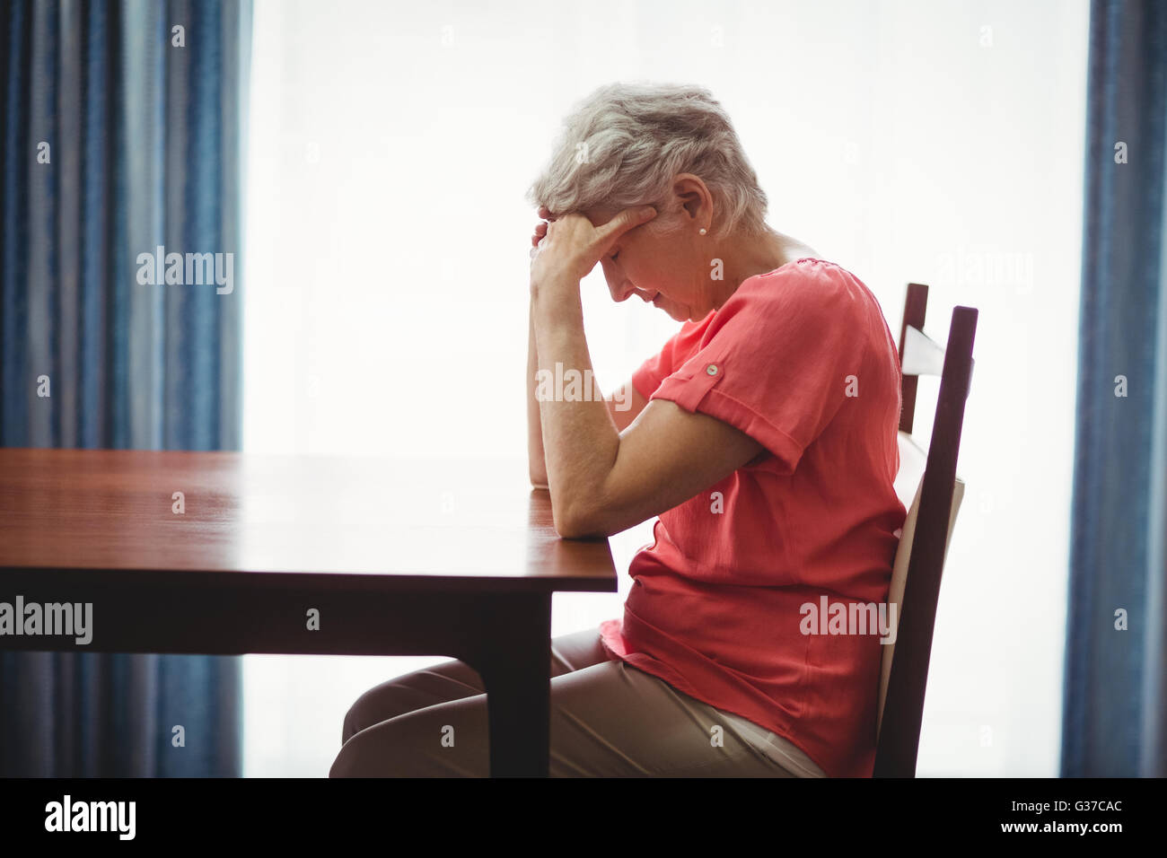 Traurige senior Frau sitzt an einem Tisch Stockfoto