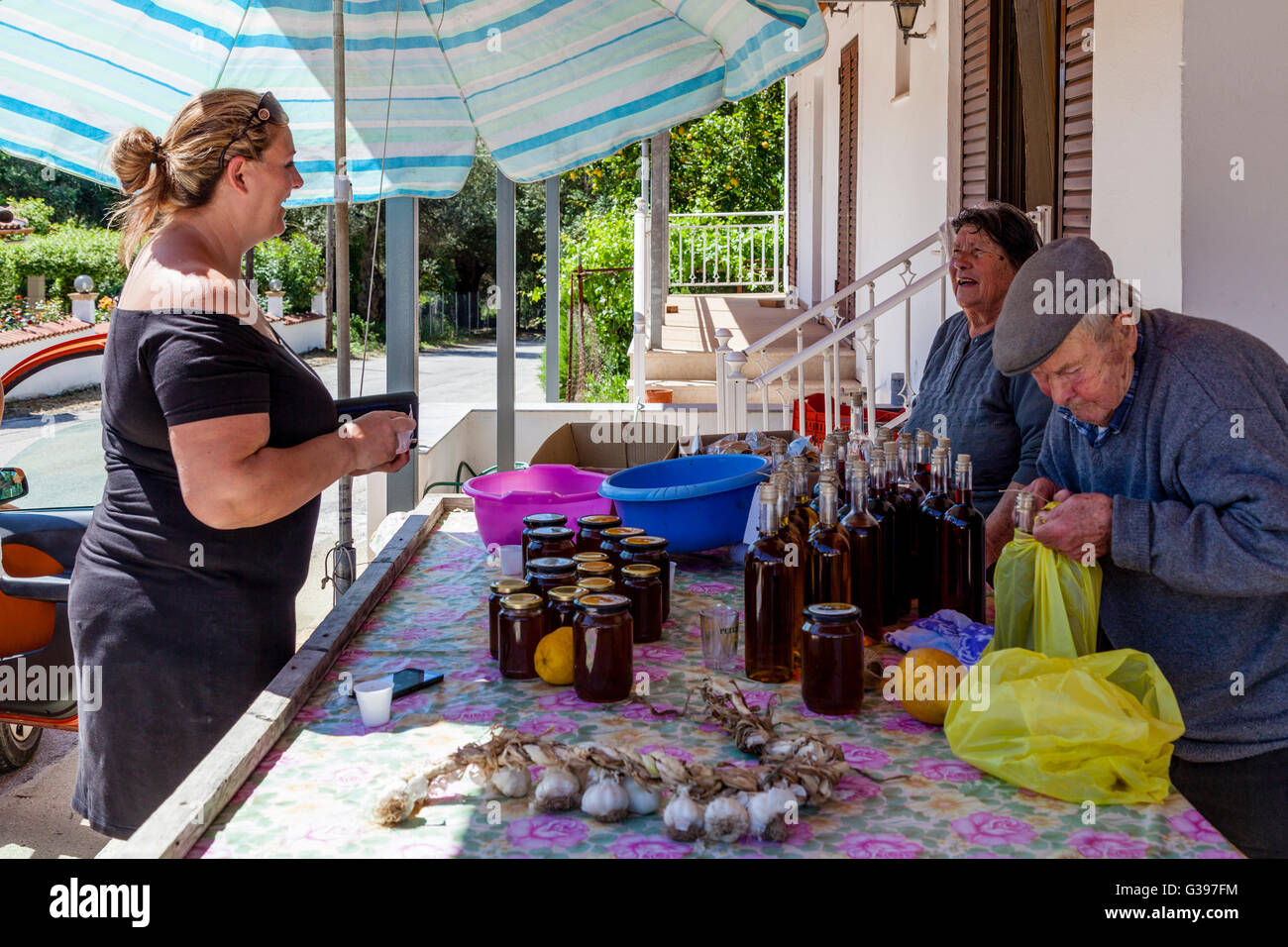 Ein weiblicher Touristen hält am Straßenrand Stall, lokale Produkte zu kaufen, von einem älteren Ehepaar, Makrades, Insel Korfu, Griechenland Stockfoto