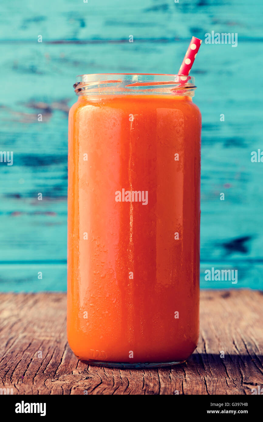 Nahaufnahme einer orange Detox-Smoothie, serviert in einem Glas mit einem roten Trinkhalm gemustert mit weißen Punkten auf einem rustikalen woode Stockfoto