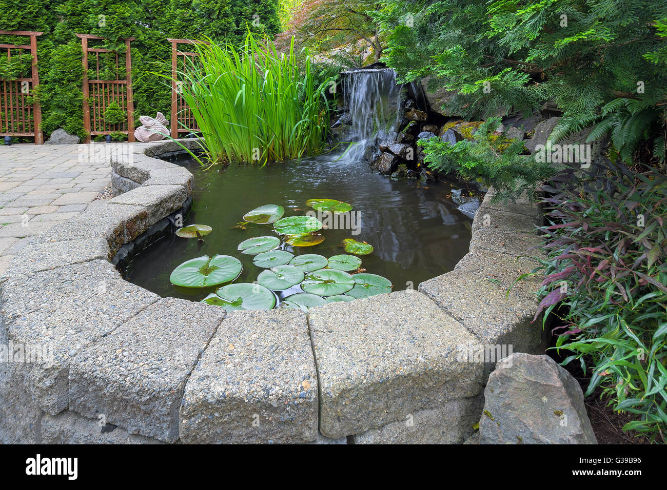 Garten-Garten-Teich mit Wasserfall Wasserpflanzen Backstein Fertiger Terrasse Landschaftsbau Spalier Stockfoto