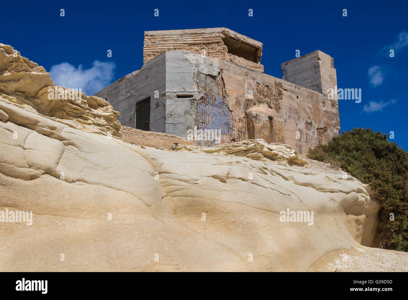 Sand Farbe der Felsen mit geschwungener Form und ein altes Gebäude. Küste der Insel Malta, Stadt Marsaskala. Blauer Himmel mit einigen whi Stockfoto