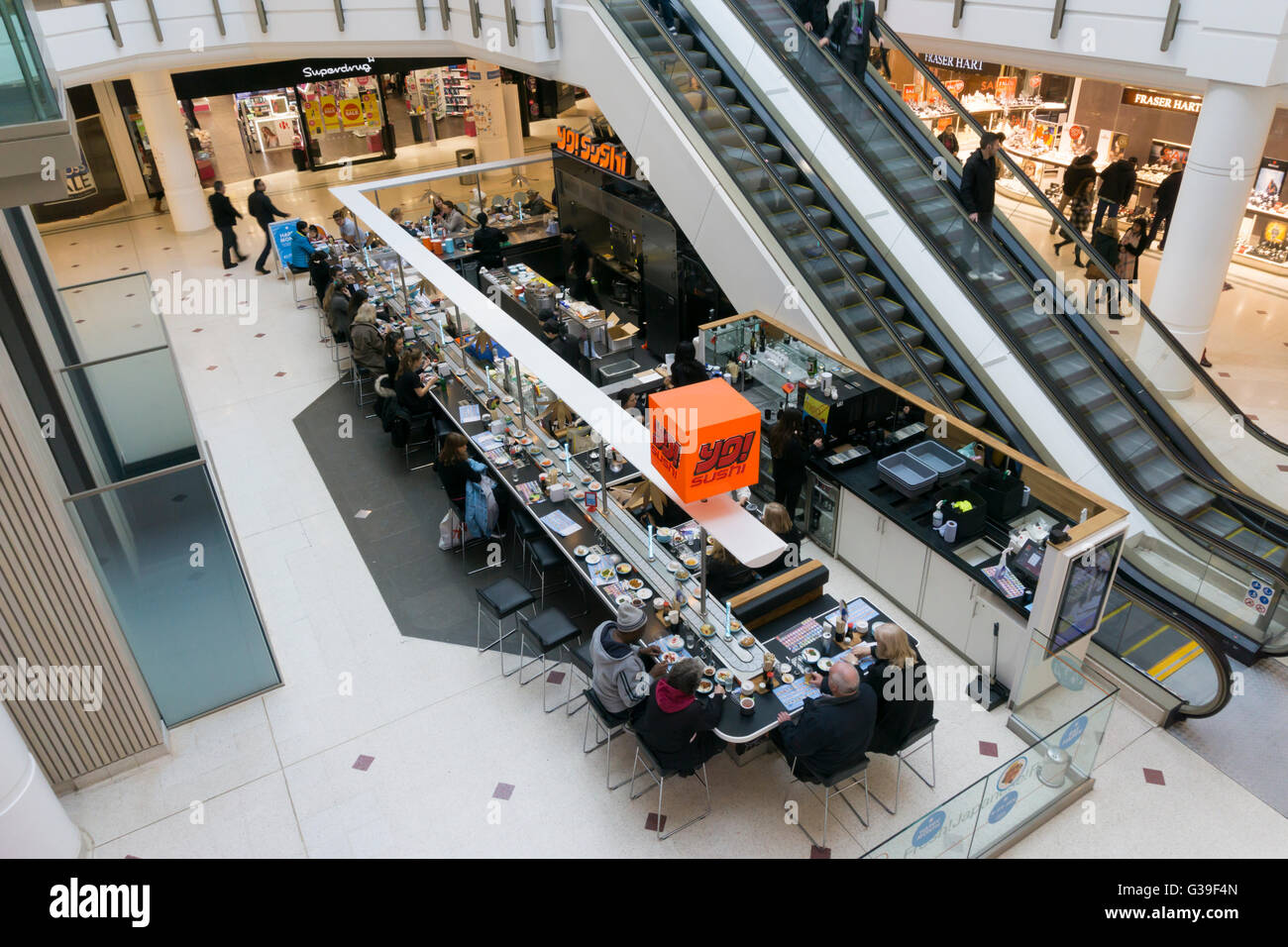 Menschen essen japanisches Essen bei einer Filiale der Yo! Sushi in Shopping-Mall in Bromley mit Schüsseln mit Essen vorbei am laufenden Band. Stockfoto