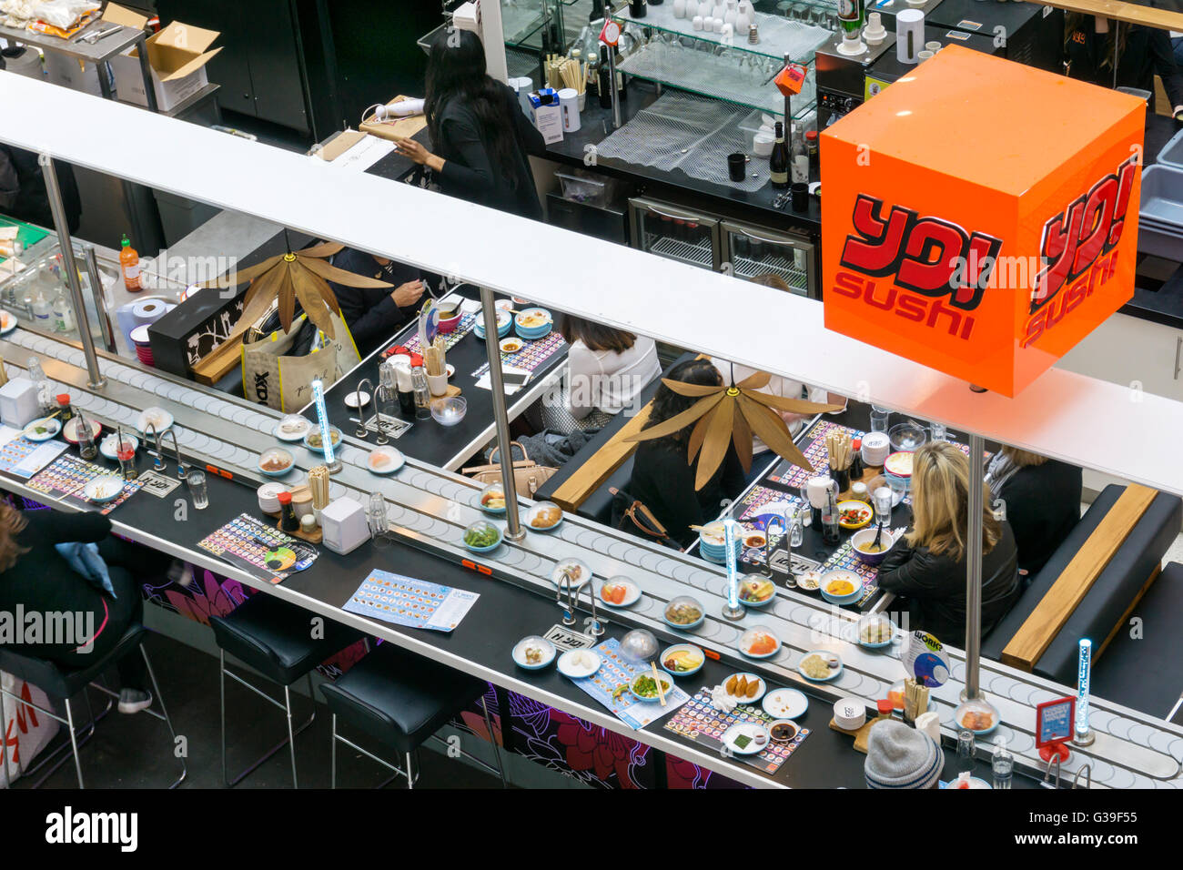 Menschen essen japanisches Essen bei einer Filiale der Yo! Sushi in Bromley mit Schüsseln mit Essen vorbei am laufenden Band. Stockfoto