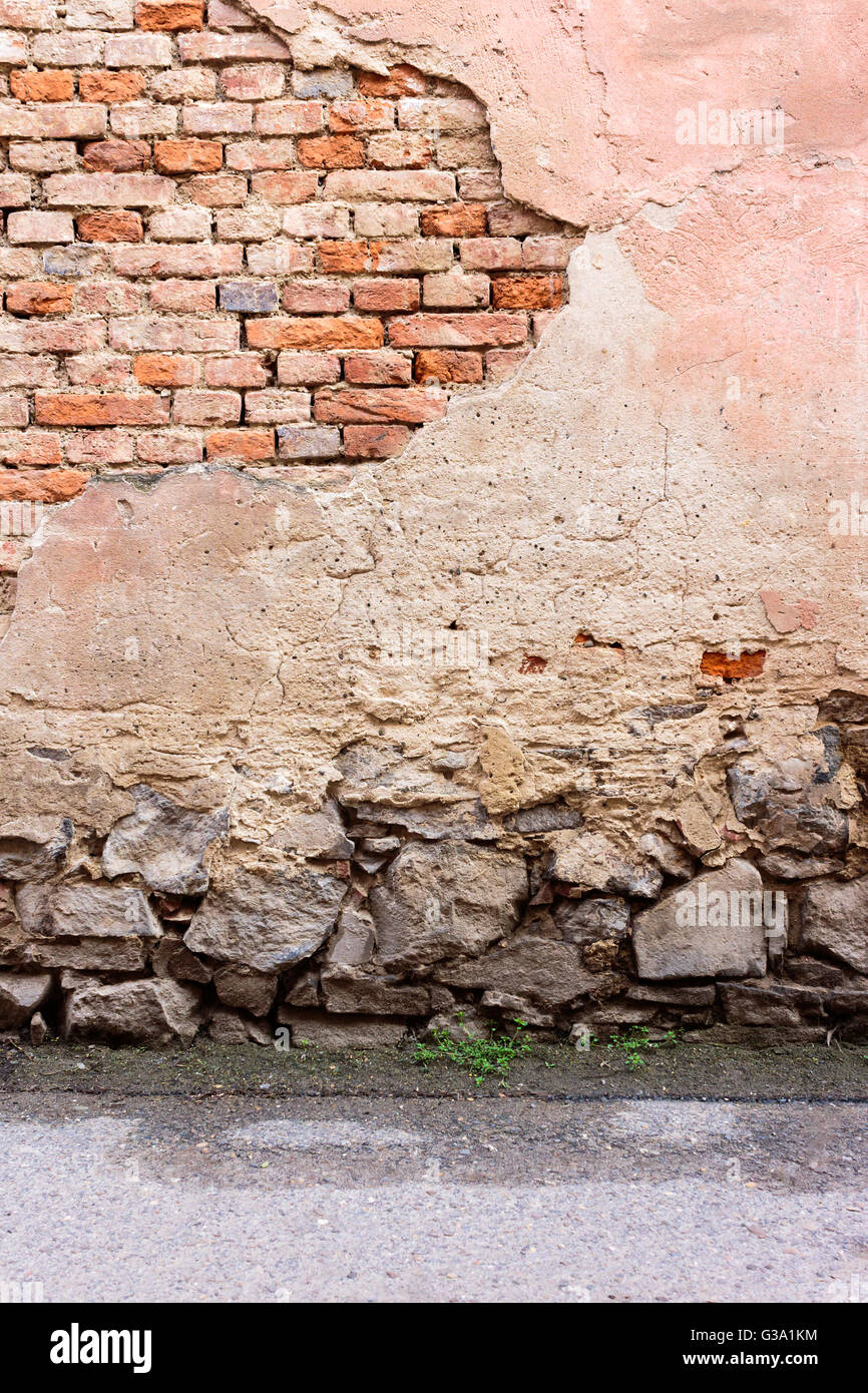 Ziegelwand mit angeschlagenen Putz, Steinfundament und Asphaltstraße Stockfoto