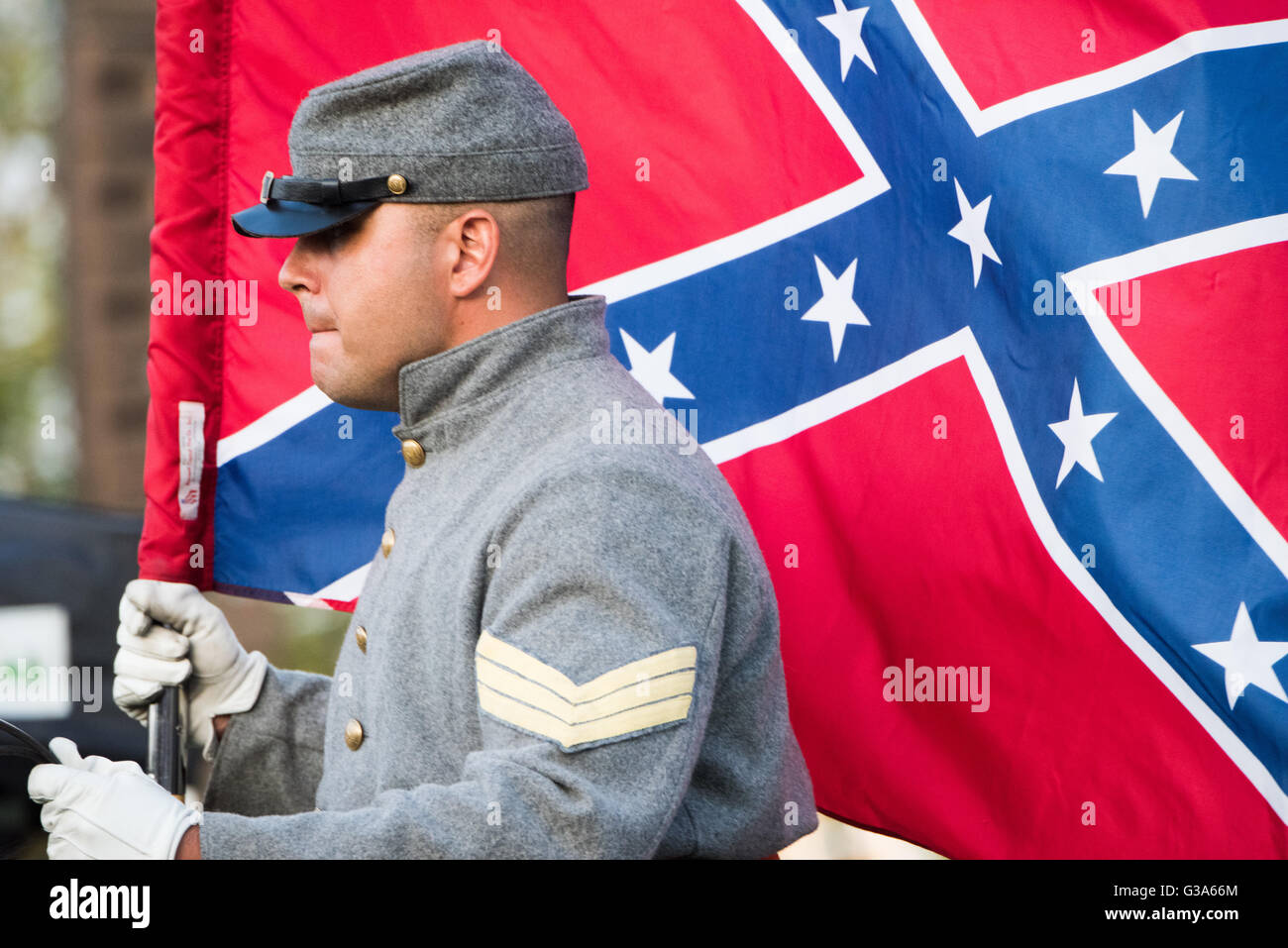 ARLINGTON, Virginia — Eine konföderierte Schlachtflagge, auch bekannt als Southern Cross, wird von einer Person gehalten, die als konföderierter Soldat aus dem Amerikanischen Bürgerkrieg gekleidet ist. Der Soldat trägt eine graue Uniform mit goldenen Knöpfen, gelben Chevrons, die den Rang anzeigen, einen Kepi und weiße Handschuhe, die mit der Kleidung der Konföderierten Armee übereinstimmen. Diese Bilder werden häufig bei historischen Nachstellungen oder Gedenkveranstaltungen gesehen. Die Confederate Battle Flag ist ein historisch bedeutendes und oft kontroverses Symbol der Konföderierten Staaten von Amerika. Diese Szene findet statt Stockfoto