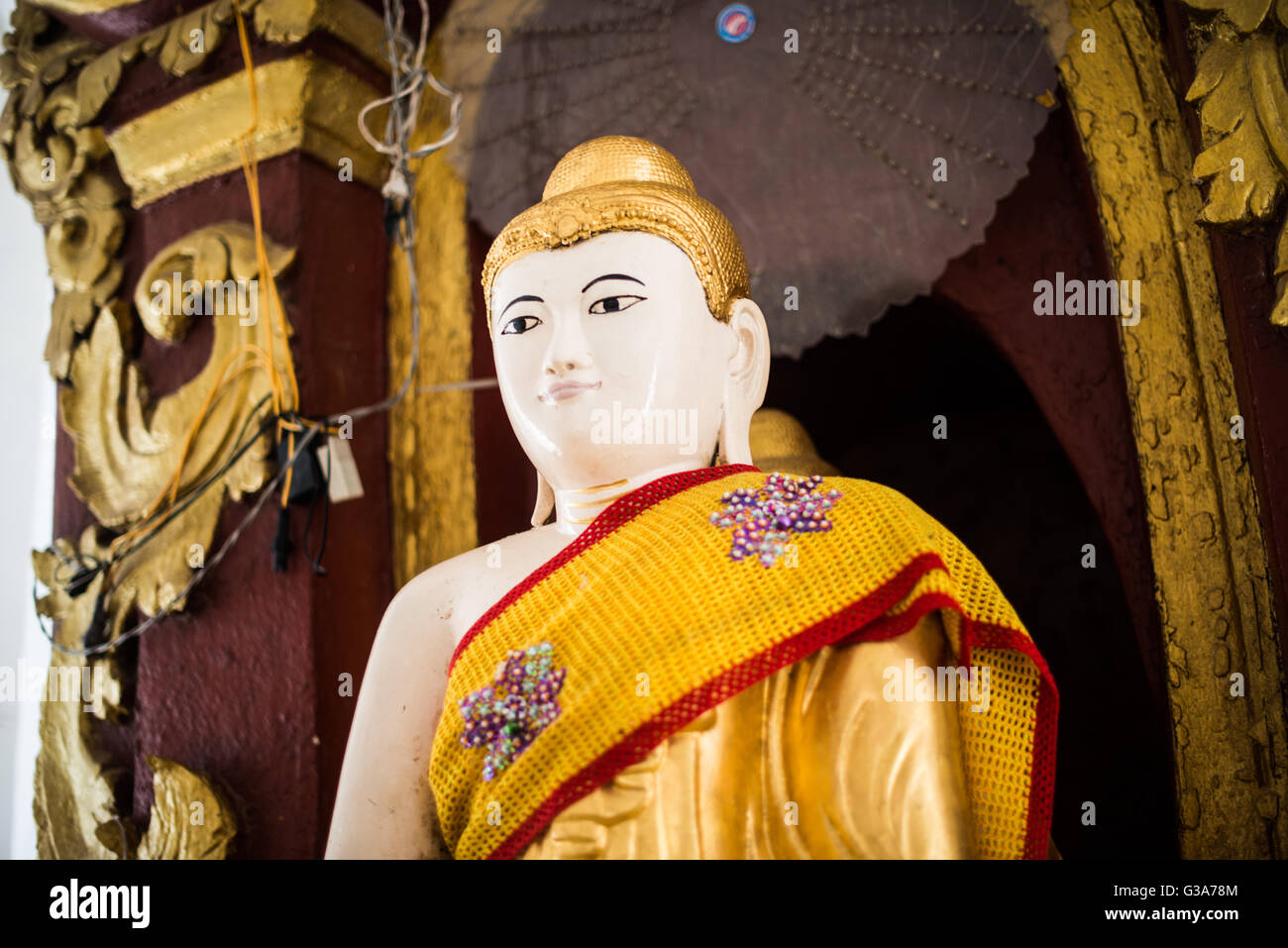Buddha Statue Hsinbyume Pagoda Mingun Myanmar // MINGUN, Myanmar — Eine Buddha-Statue mit weißen Blumenopfern befindet sich in der Hsinbyume Pagoda, auch bekannt als Myatheindan Pagoda. Die Pagode wurde 1816 von Prinz Bagyidaw als Denkmal für seine erste Frau, Prinzessin Hsinbyume, erbaut, die bei der Geburt starb. Die markante weiße Struktur repräsentiert den Mount Meru, den heiligen Berg im Zentrum des Universums in der buddhistischen Kosmologie, mit seinen sieben terrassenförmig angelegten Ebenen, die die sieben Bergketten rund um den mythischen Gipfel symbolisieren. Gelegen am westlichen Ufer des Ayeyarwady River in der Nähe von Mandala Stockfoto