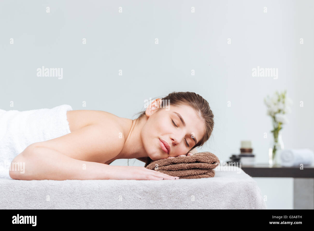 Zärtliche junge Frau auf Handtuch liegend mit Augen geschlossen während der Hautpflege im Wellness-salon Stockfoto