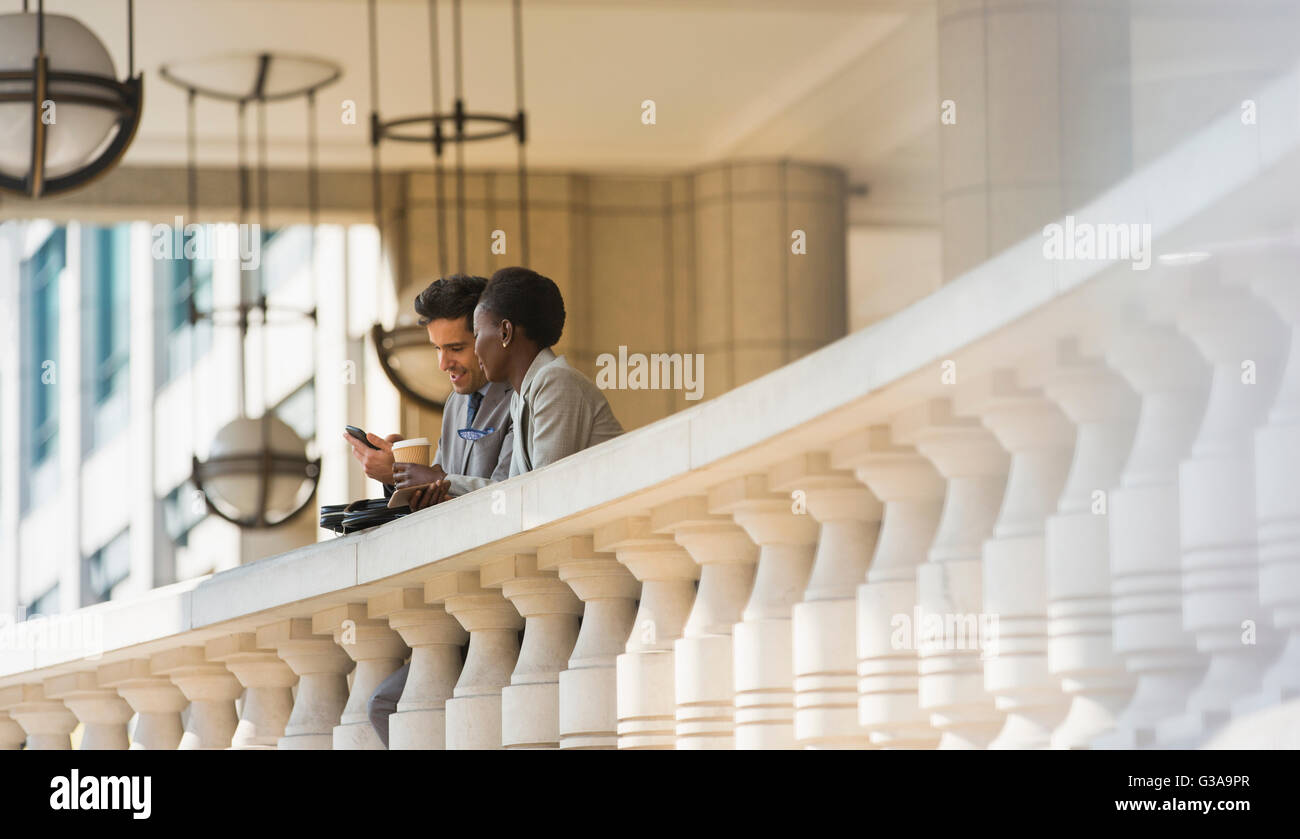Corporate Geschäftsmann und Geschäftsfrau mit Kaffee und Handy am Geländer Stockfoto