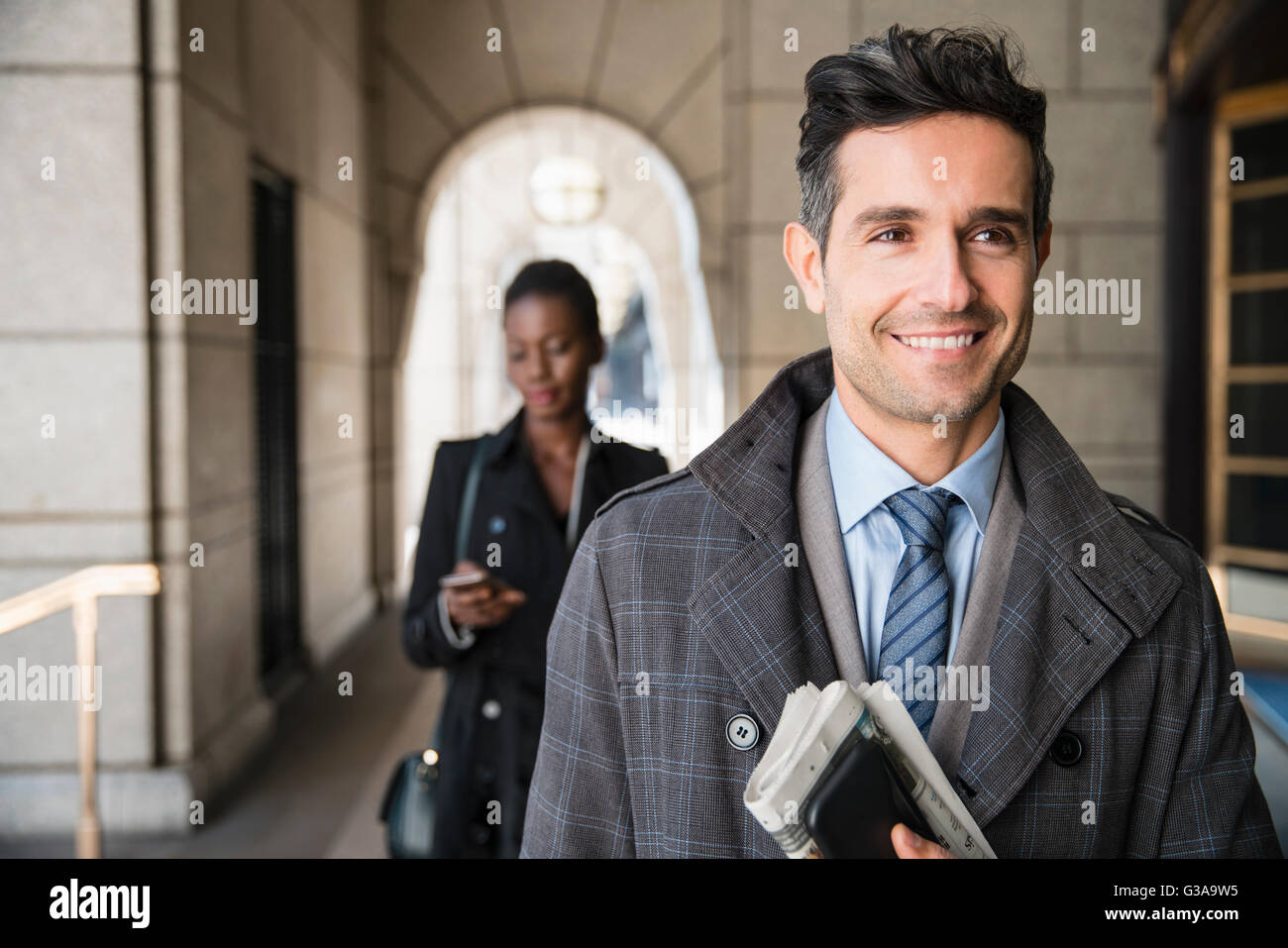 Lächelnd corporate Geschäftsmann mit Zeitung und Handy im Kreuzgang Stockfoto