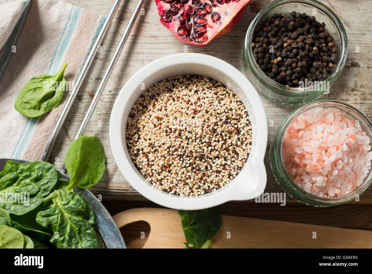 Aufwand für eine Schüssel mit Quinoa neben einer Scheibe Granatapfel, Spinat und Schüsseln mit rosa Salz und Pfefferkörner Stockfoto