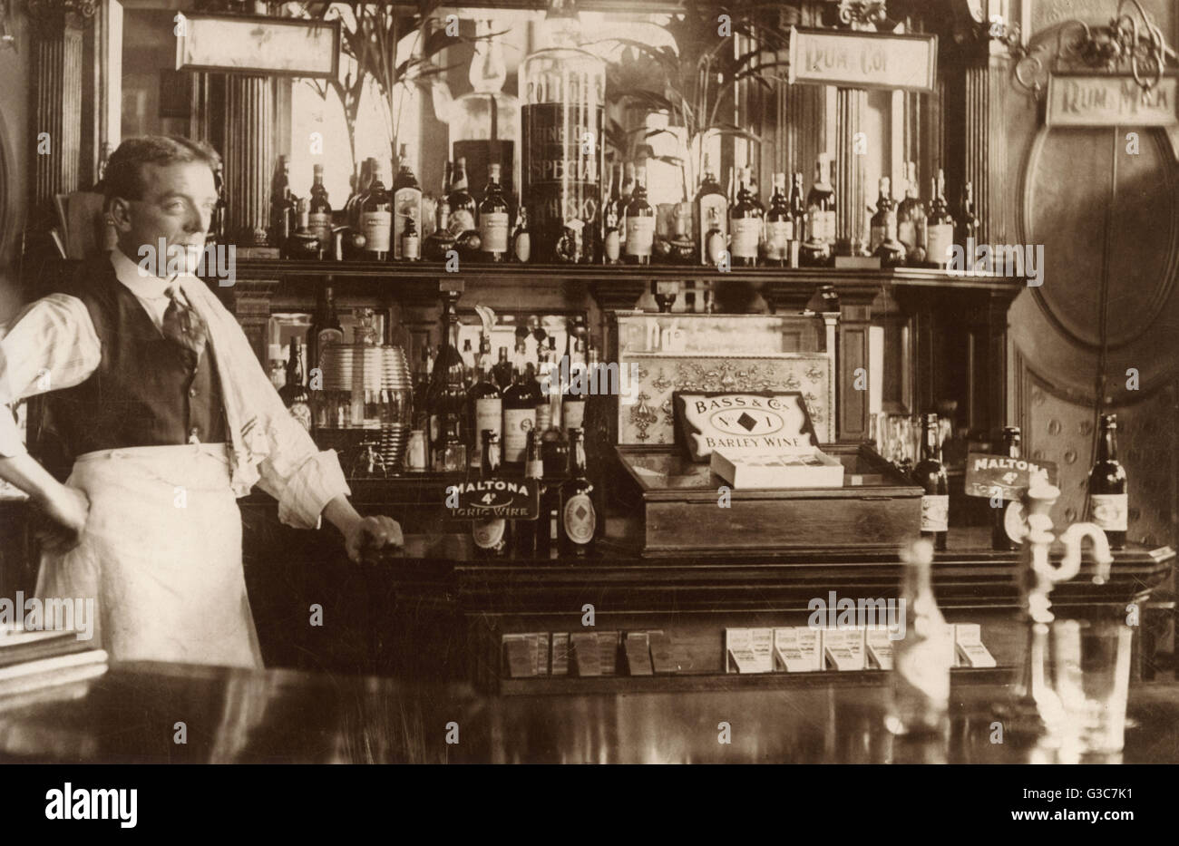 Barman steht eine gut sortierte Bar.  Die Kasse zeigt eine Anzeige für Bass &amp; Co Gerste Wein. Pakete von Capstan Zigaretten werden auf dem Display unten.      Datum: um 1910 Stockfoto