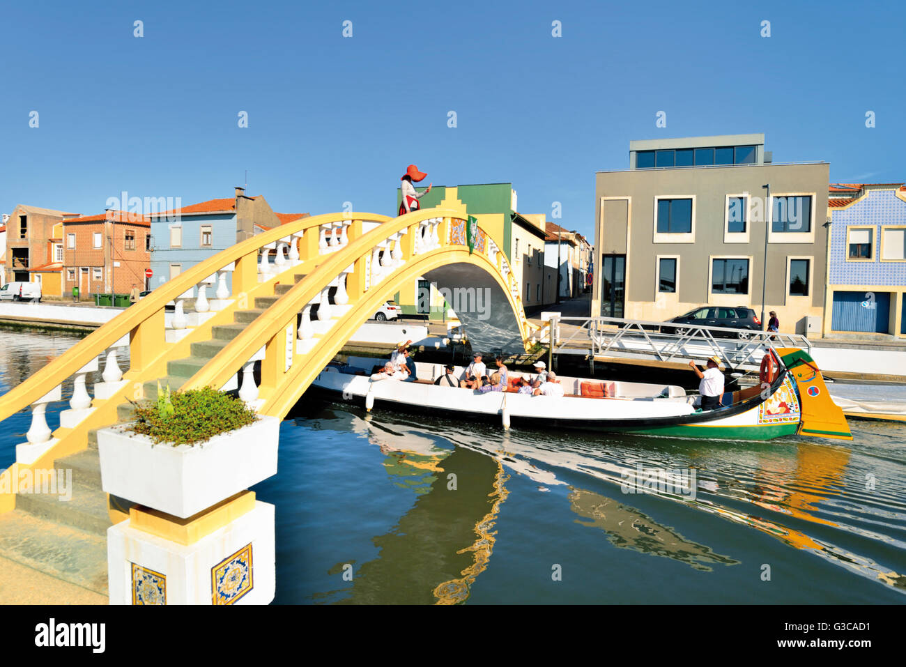 Portugal, Aveiro: Traditionelle Moliceiro Boot vorbei an Canal de Sao Roque unter Kanal-Brücke mit Frau winken für Touristen Stockfoto