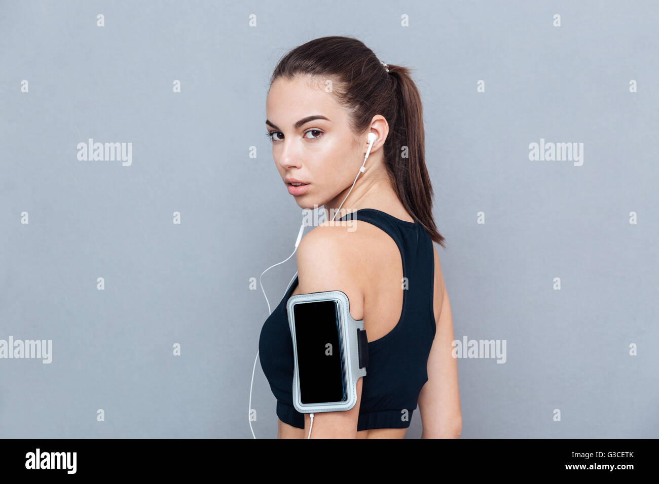 Close-up Portrait von einem Fitness He Lthy schönes Mädchen mit Smartphone und Kopfhörern auf grauem Hintergrund isoliert Stockfoto