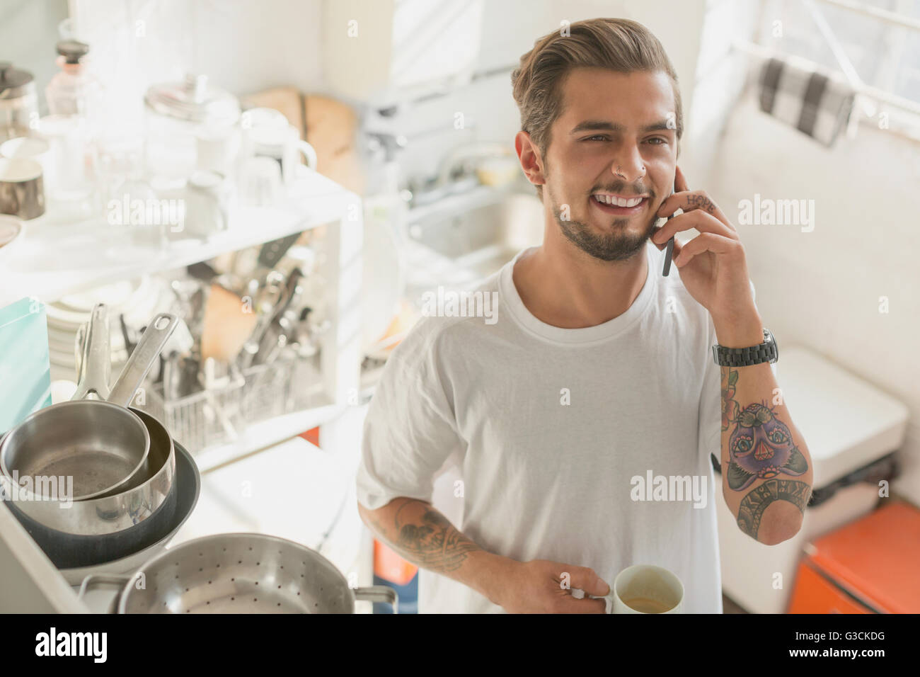 Tätowierte junge Mann reden über Handy und Kaffeetrinken in Küche Stockfoto