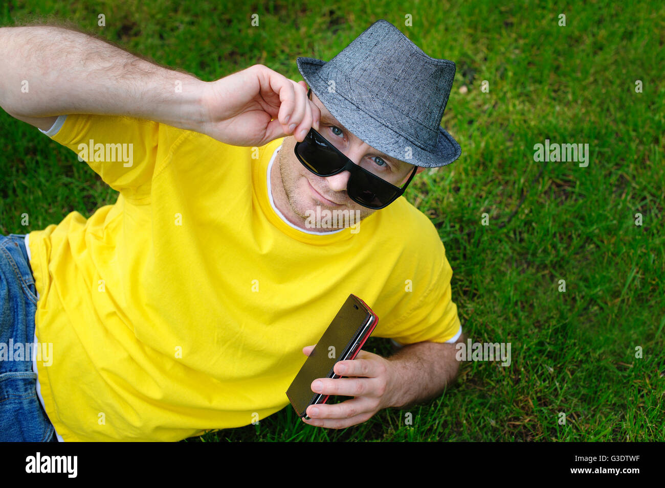 Mann trägt einen Hut mit dem Telefon auf dem Rasen liegend Stockfoto