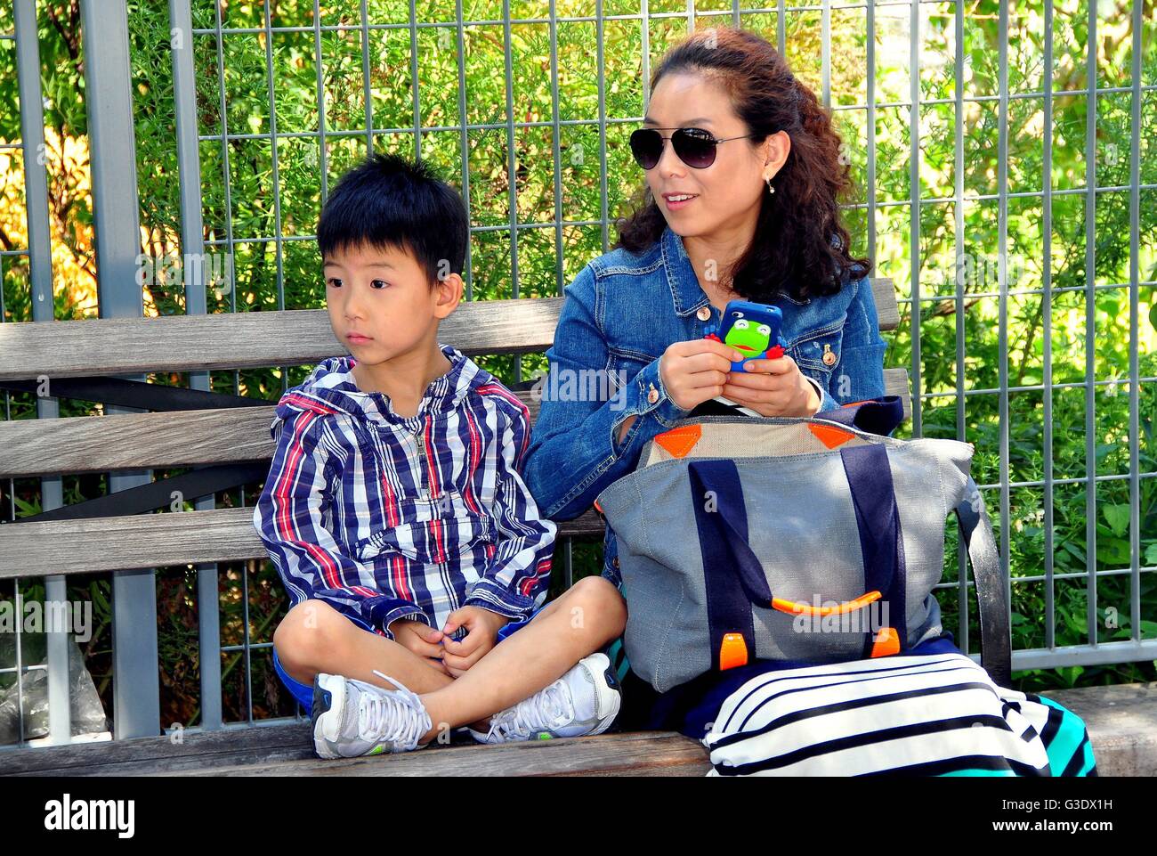New York City: Asiatische Mutter und ihrem kleinen Sohn entspannend auf einer Parkbank am Pier 84 auf dem Hudson River Stockfoto