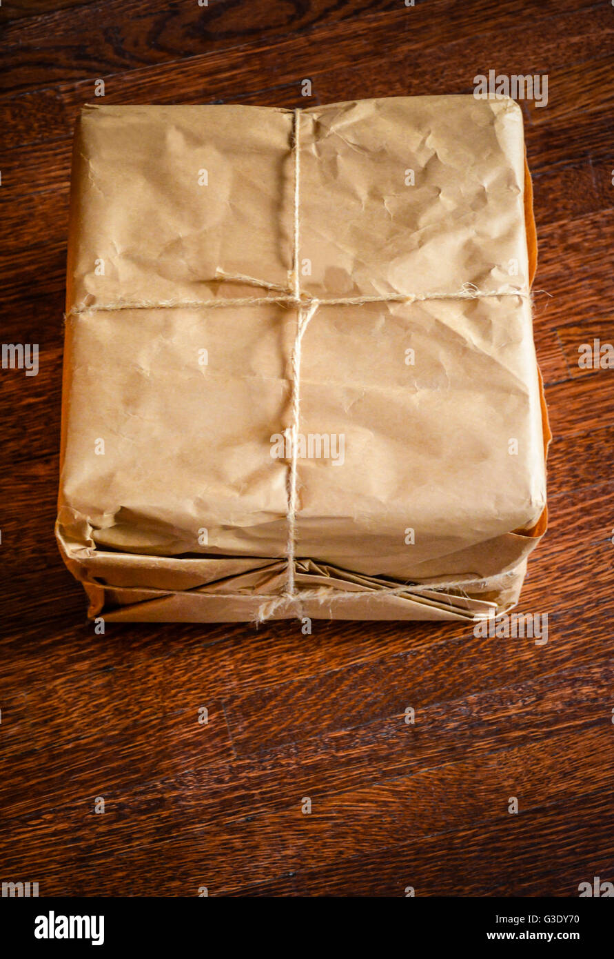 Braune Normalpapier verpackte Paket mit Paket Schnur sitzt auf einem hölzernen Parkettboden, unadressierte und etwas Geheimnisvolles Stockfoto
