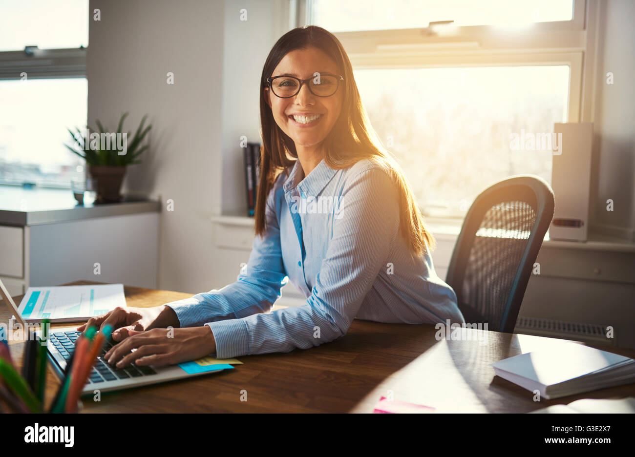 Unternehmerin am Schreibtisch lächelt in die Kamera, blaue warme Farben Stockfoto
