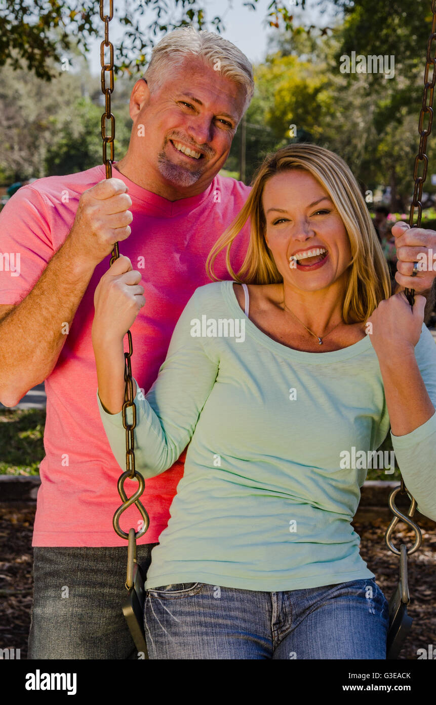 reifer Mann schob seine jüngere Frau auf einer Schaukel Stockfoto