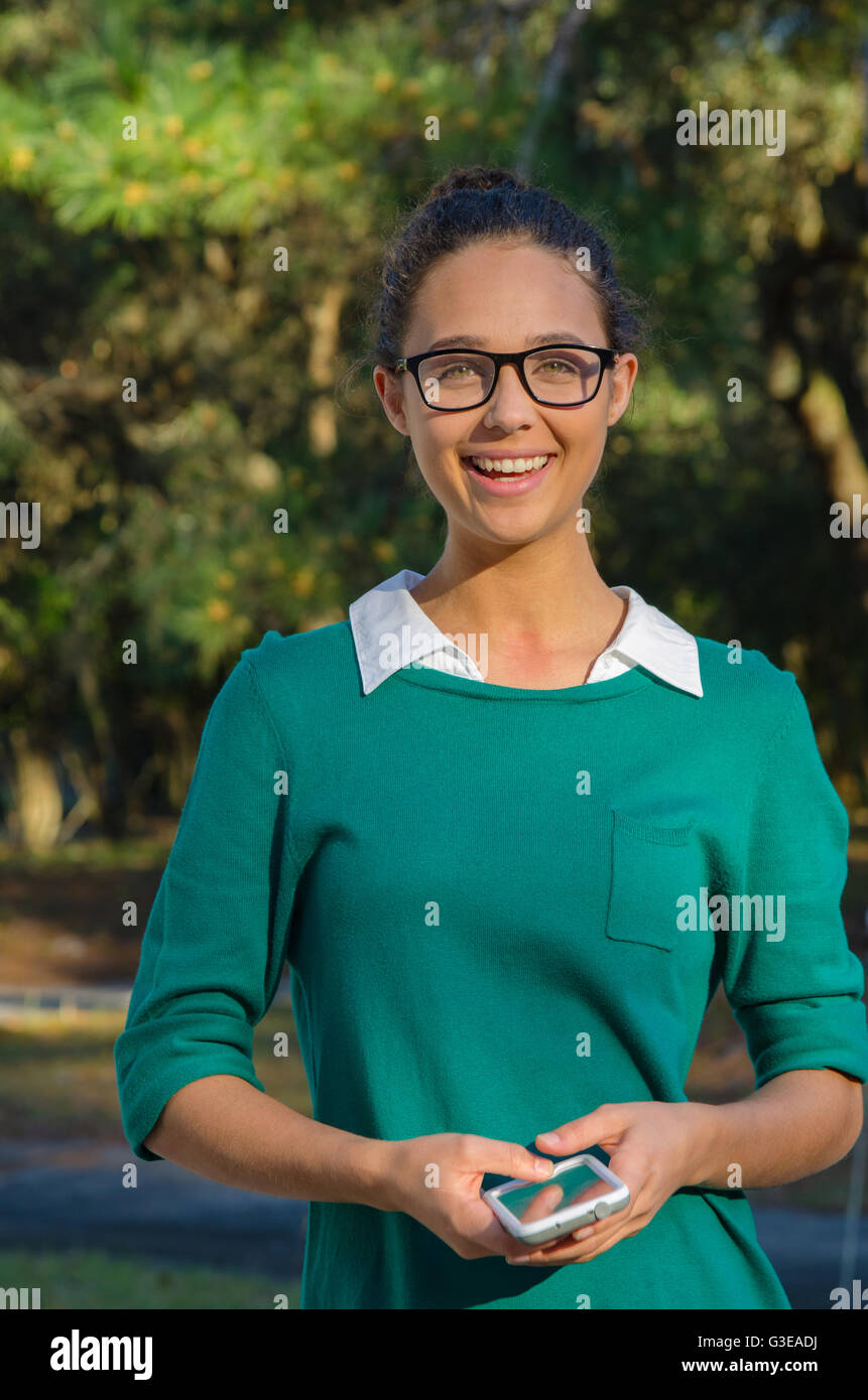 Bi-Rasse junge Frau lächelnd außerhalb lässig in Brille hält ein Handy Stockfoto