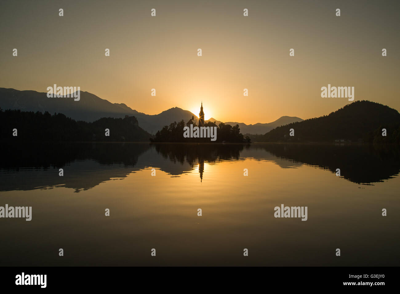 Kirche Mariä Himmelfahrt am Bleder See bei Sonnenaufgang. Hügel und Berge werden können die Entfernung zu sehen. Stockfoto
