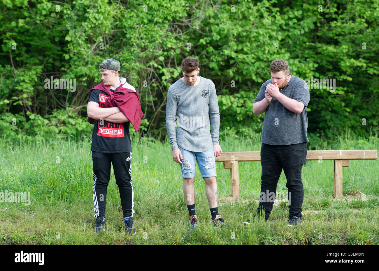 Drei junge Männer stehen und blicken in einen Wald Teich, einen über Gewicht und Rauchen. Stockfoto