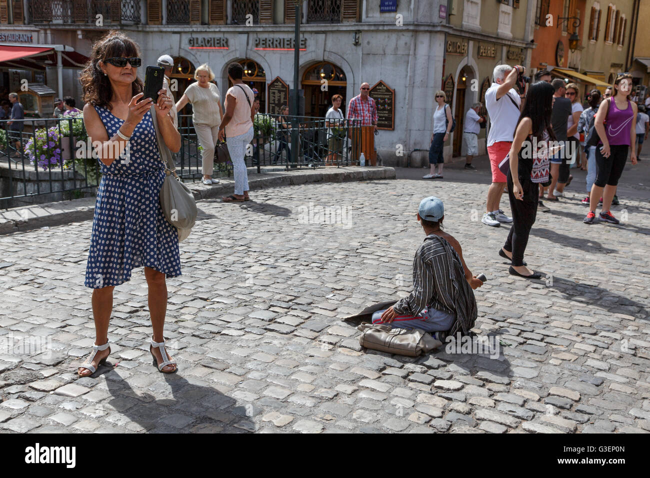 Ein Tourist fotografiert neben einem Bettler in Annecy, Haute-Savoie, Rhône-Alpes, Frankreich Stockfoto
