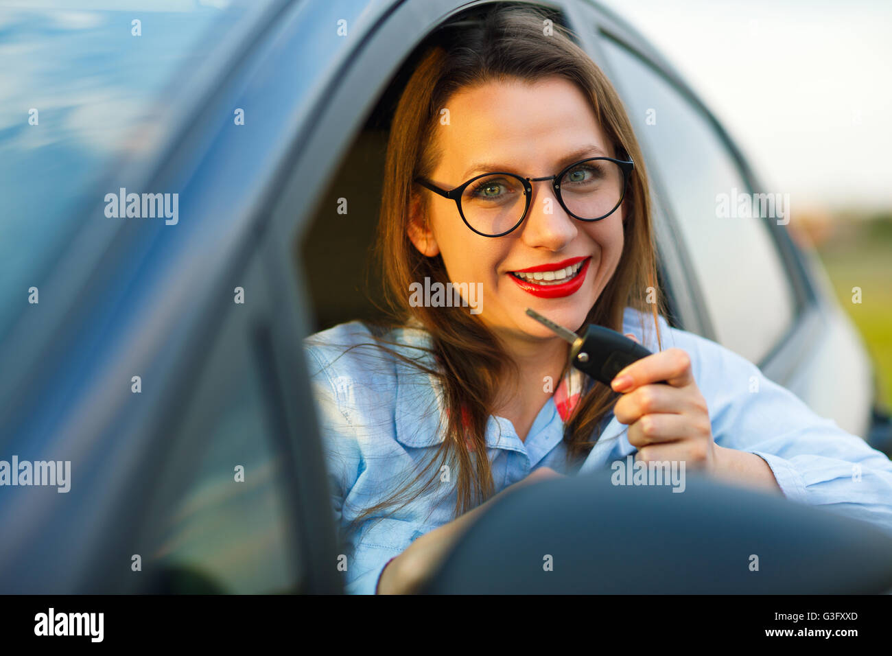 Junge hübsche Frau sitzt in einem Auto mit dem Schlüssel in Hand - Konzept für den Kauf eines Gebrauchtwagens oder einen Mietwagen Stockfoto