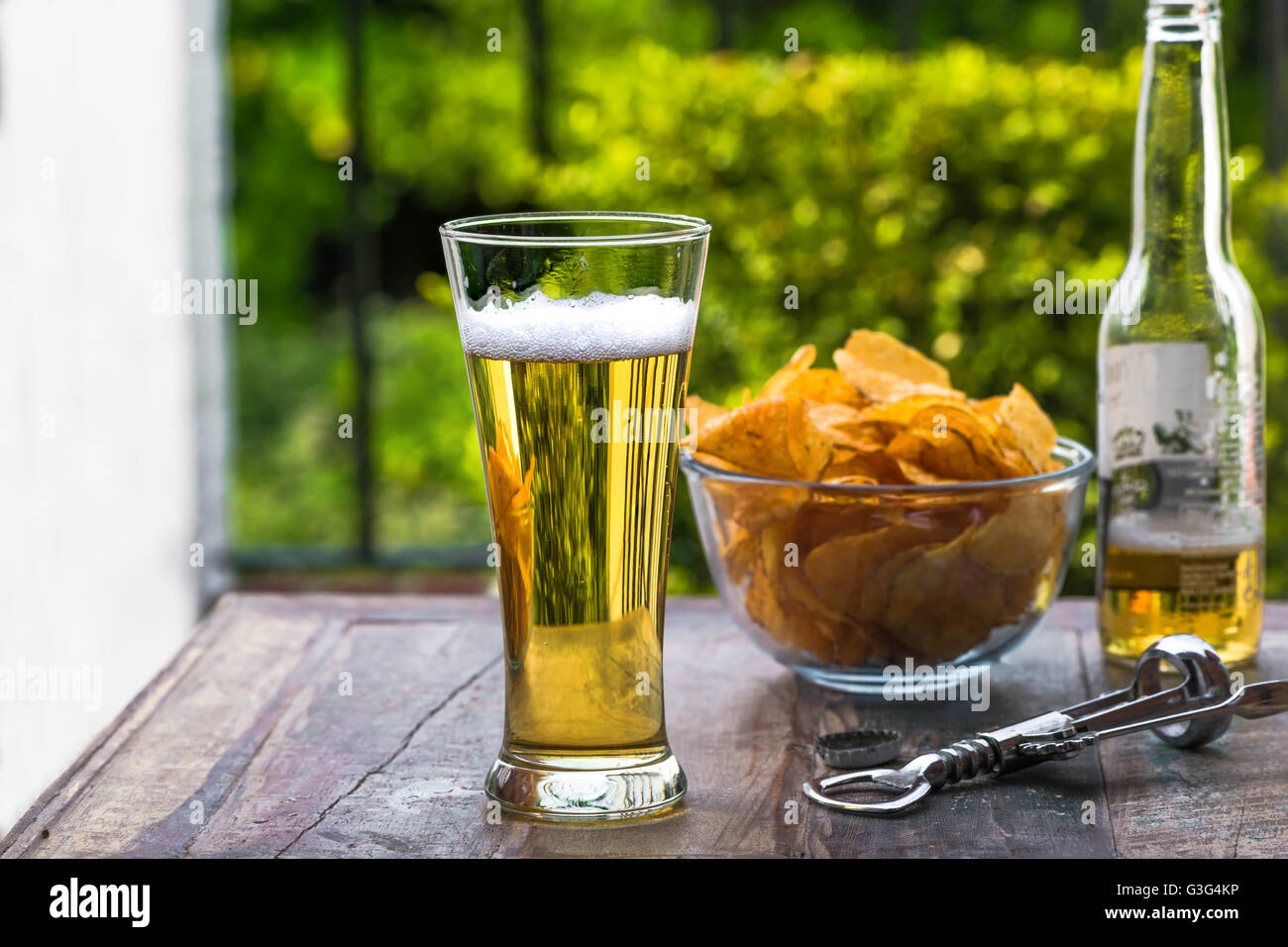 Ein Glas Bier und eine Schüssel mit Chips auf einem Tisch im Garten Stockfoto