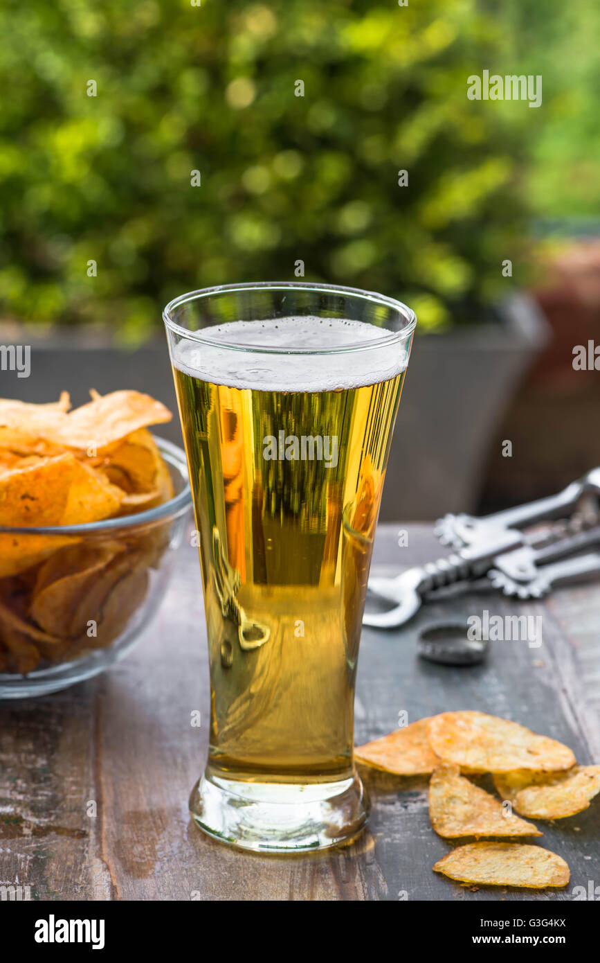 Ein Glas Bier und eine Schüssel mit Chips auf einem Tisch im Garten Stockfoto