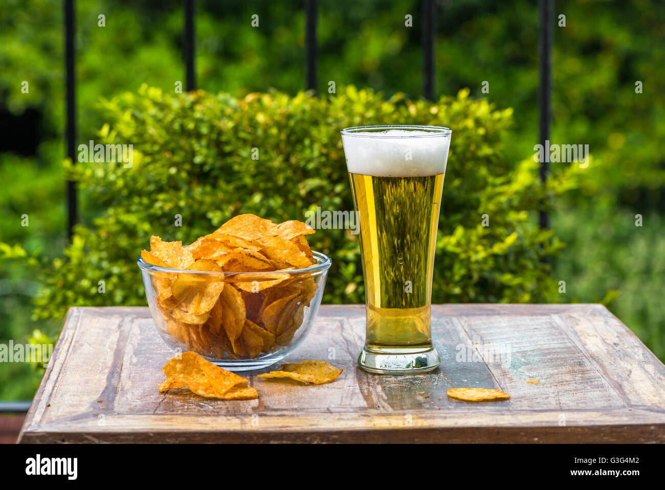 Ein Glas Bier und eine Schüssel mit Chips auf einem Tisch im Garten Stockfoto