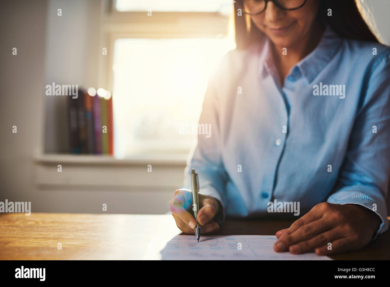 Selektiven Fokus auf den Händen der einzelnen Frau in blauen Bluse arbeiten am Schreibtisch auf Schreibarbeit im home-Office mit Sonnenlicht über ihre Schulter Stockfoto