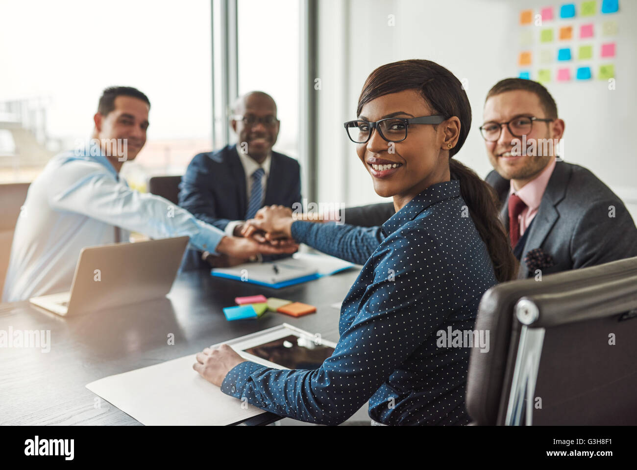 Erfolgreichen afroamerikanischen Teamleiter drehen, um in die Kamera zu Lächeln, als ihr multiethnischen Team von Führungskräften Links Hände über Stockfoto