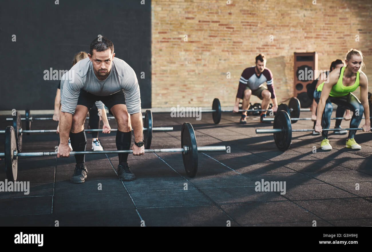 Passen Sie jungen Mann Aufhebung Hanteln suchen konzentriert, trainieren Sie im Fitnessraum mit anderen Menschen Stockfoto