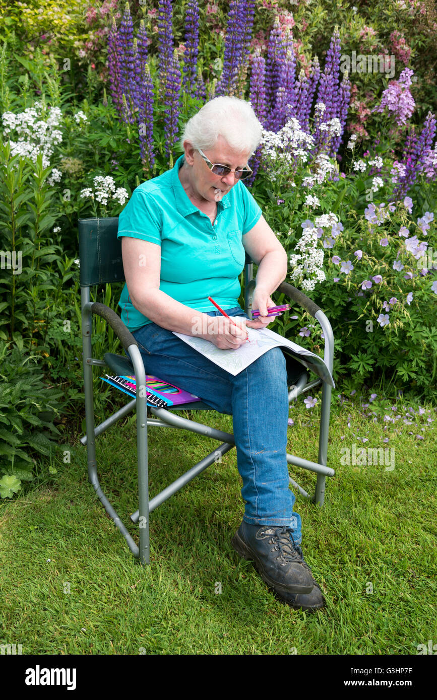 Reife Frau sitzen im Garten mit einem Erwachsenen Malbuch. Stockfoto