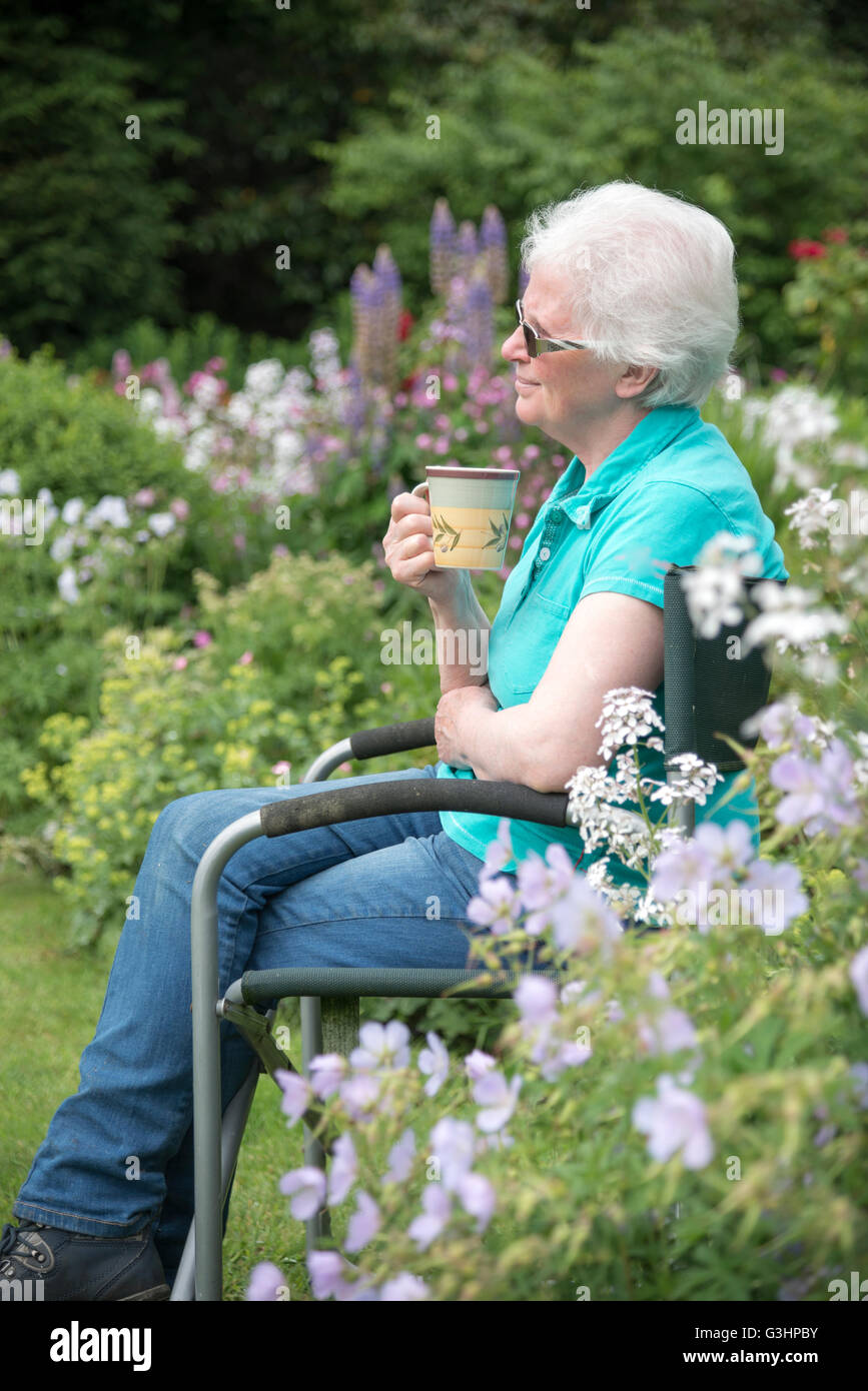 Reife Dame saß im Garten mit Tasse Tee und einen durchdachten, reflektierende Ausdruck auf ihrem Gesicht. Stockfoto