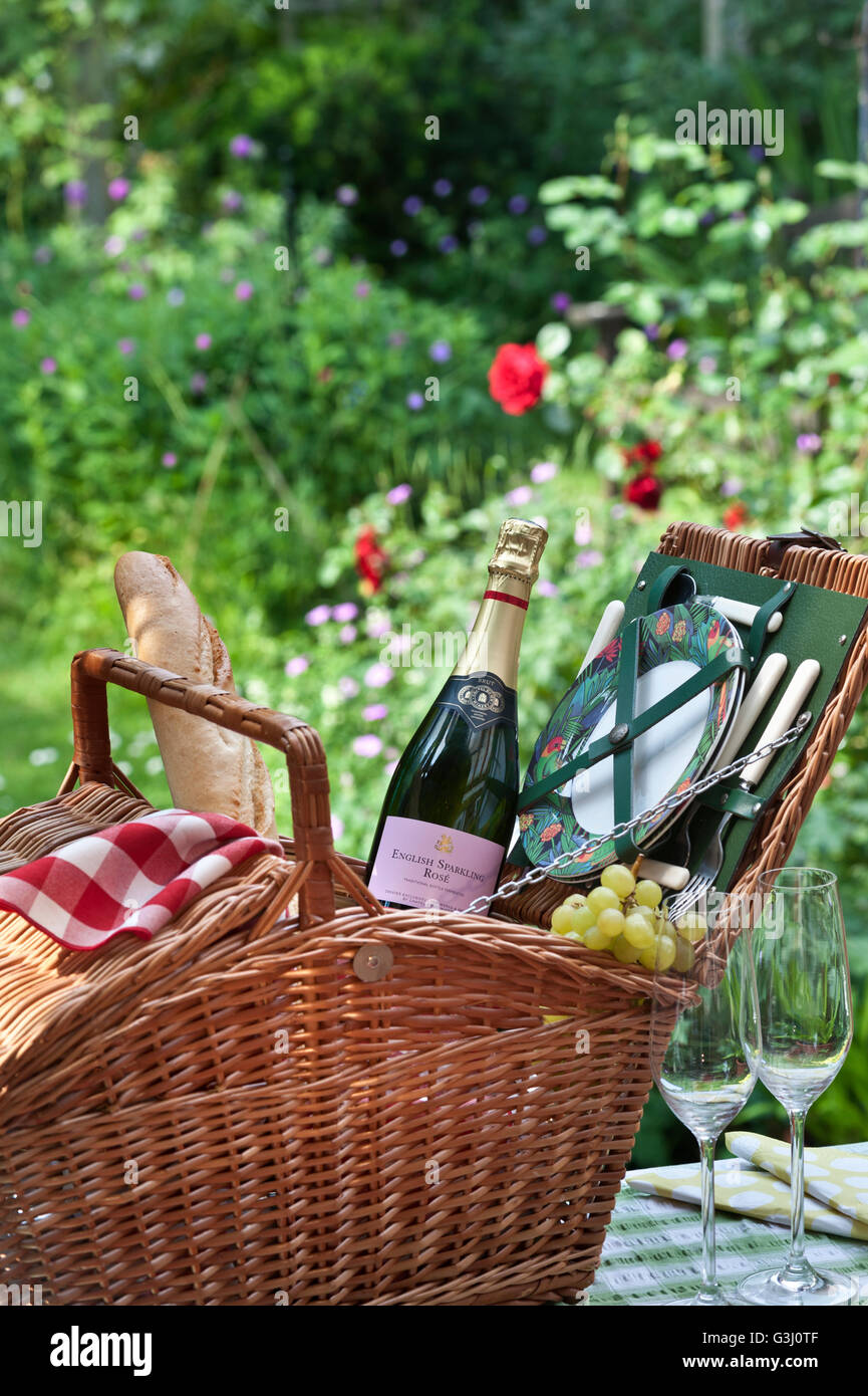 Englischer Sparkling Rosé Weinflasche und Picknickkorb mit Baguette-Frucht-Trauben in sonniger Blumengartenlage Stockfoto