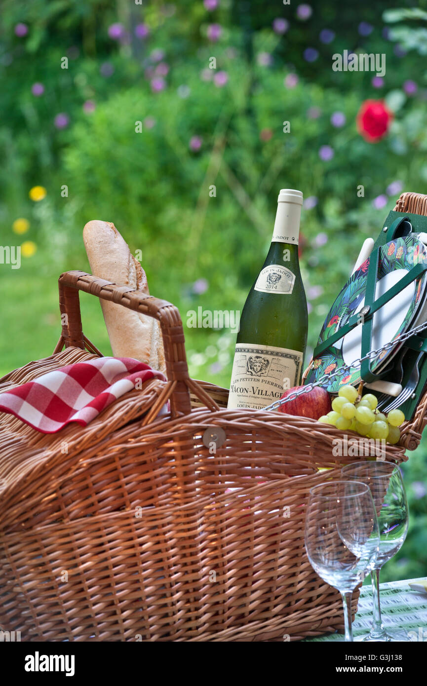 Picknickgarten Weißburgunder Weinflasche Louis Jadot Macon Dörfer und Weidenpicknickkorb in sonniger floraler Aufenthaltsgartenlage Stockfoto