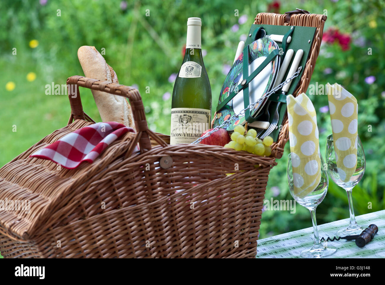 Picknickgarten Weißburgunder Weinflasche Louis Jadot Macon Dörfer und Weidenpicknickkorb in sonniger floraler Aufenthaltsgartenlage Stockfoto