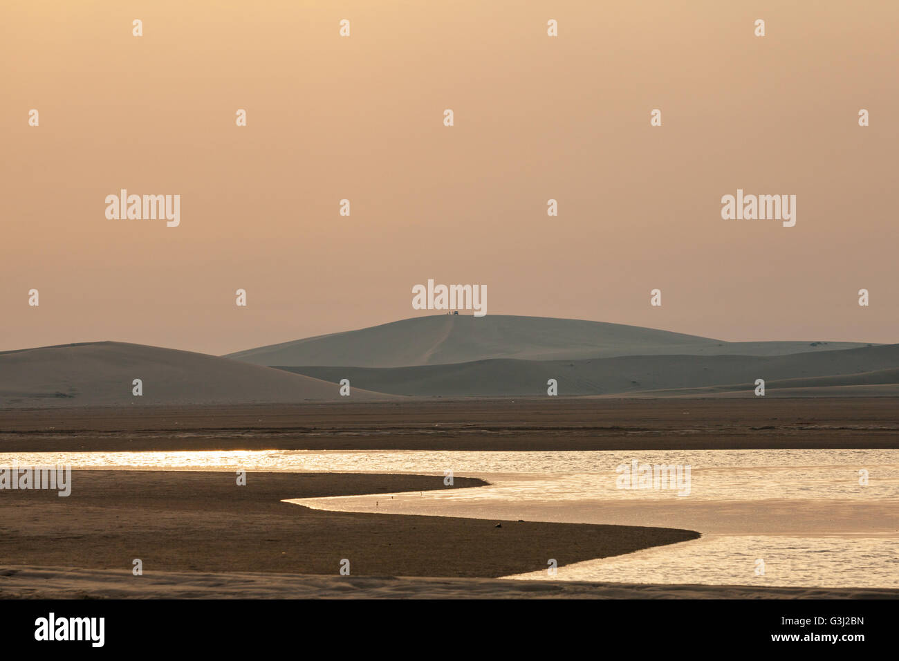 Wüste Dünen als Sonnenuntergänge vom Binnenmeer betrachtet. Menschen und SUV nur sichtbare Silhouette. Stockfoto