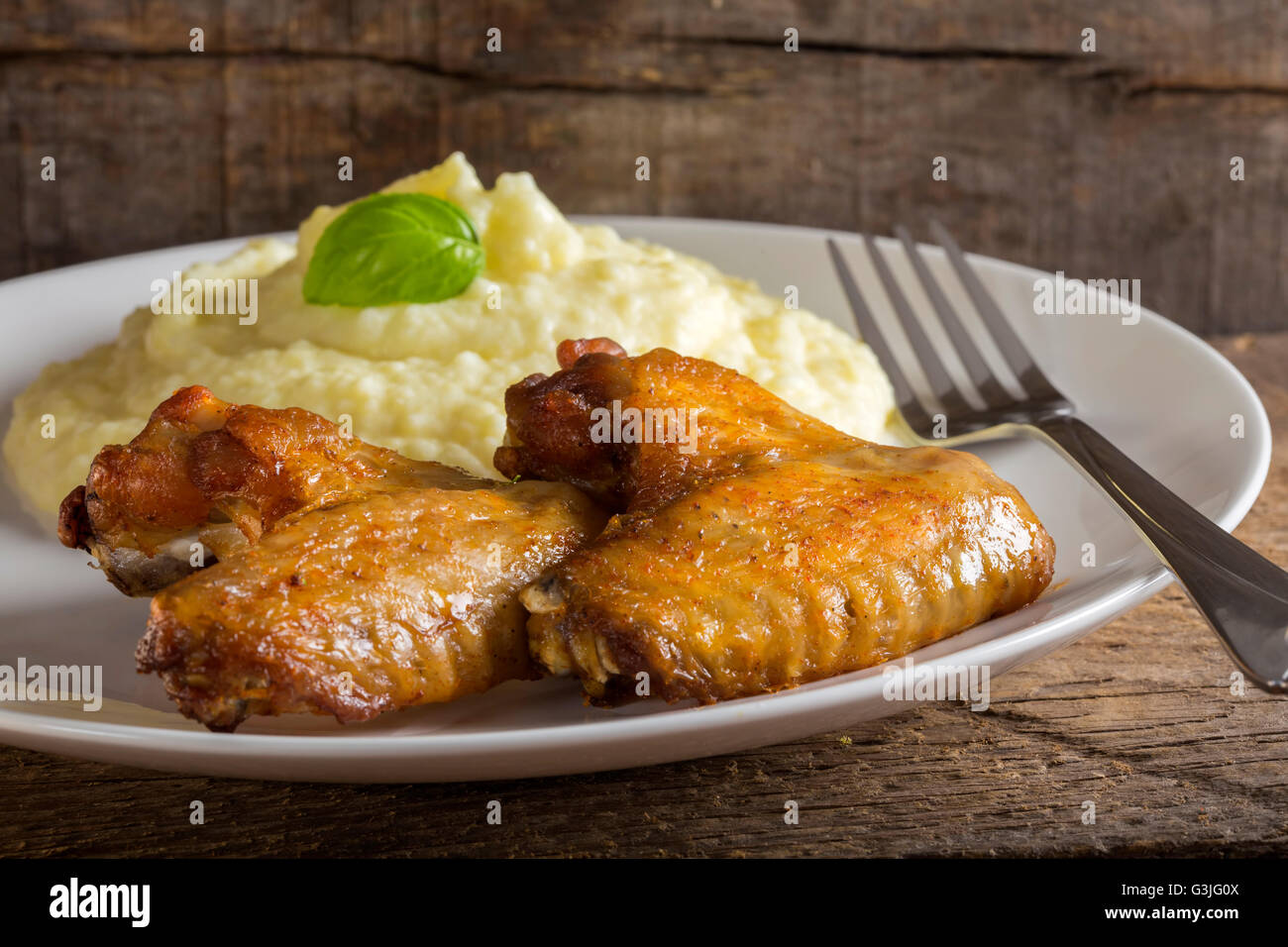 Gebratene Hähnchenflügel und gestampften Kartoffeln auf Teller mit Gabel auf hölzernen Hintergrund Stockfoto