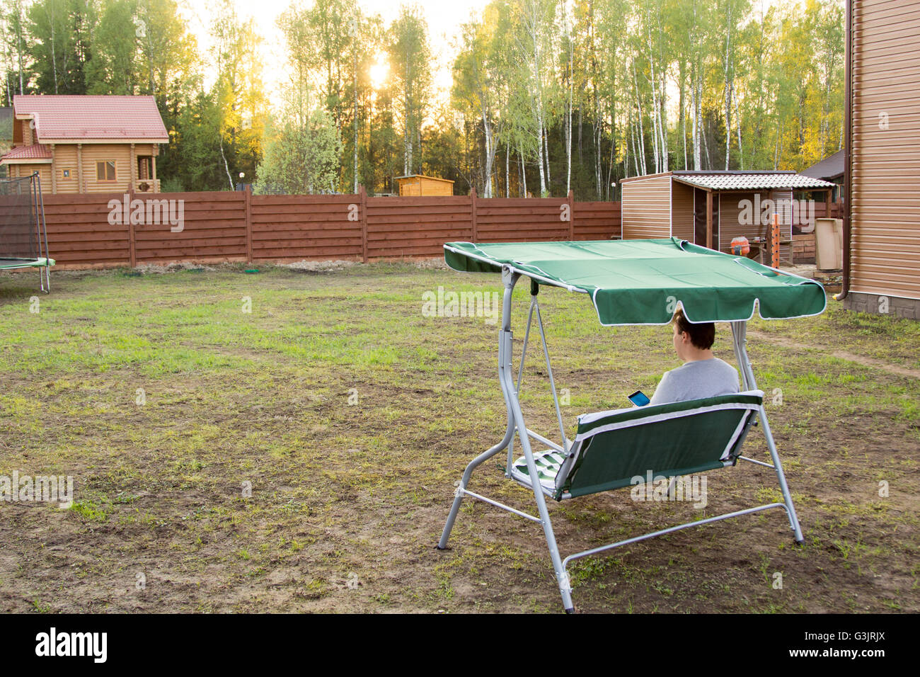 Mann sitzt auf einer Schaukel im Garten beobachten Sonnenuntergang Stockfoto