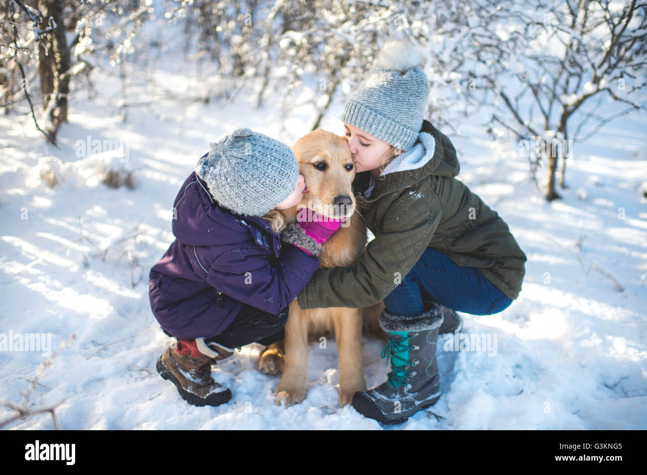 Zwei junge Mädchen, Hund, in verschneiter Landschaft umarmen Stockfoto